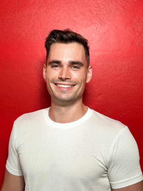 Felix H Mohr smiling in a white T-shirt against a red backdrop
